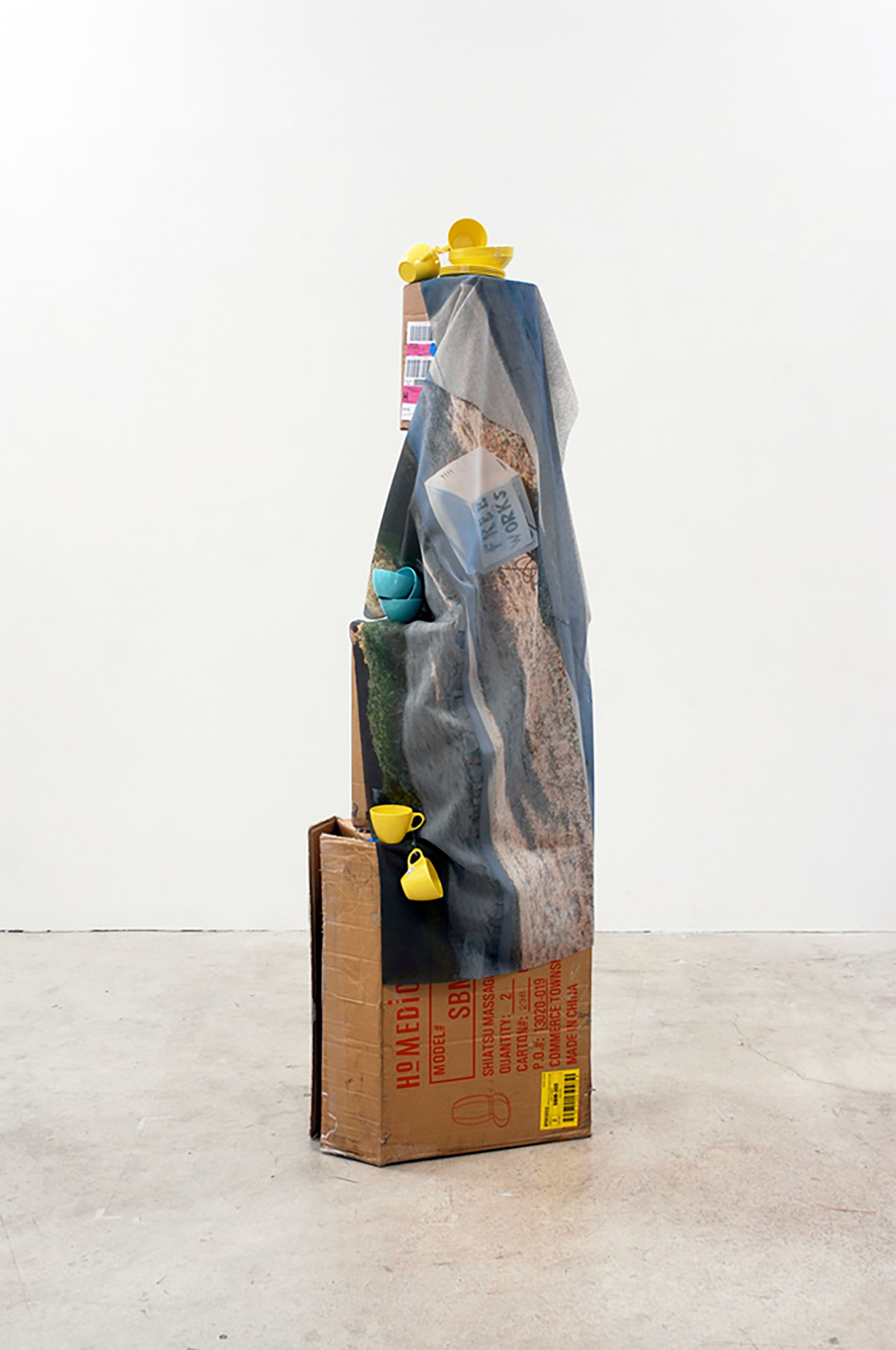 Box with blue and grey blanket draped over with with yellow plastic dinnerware balanced on top.
