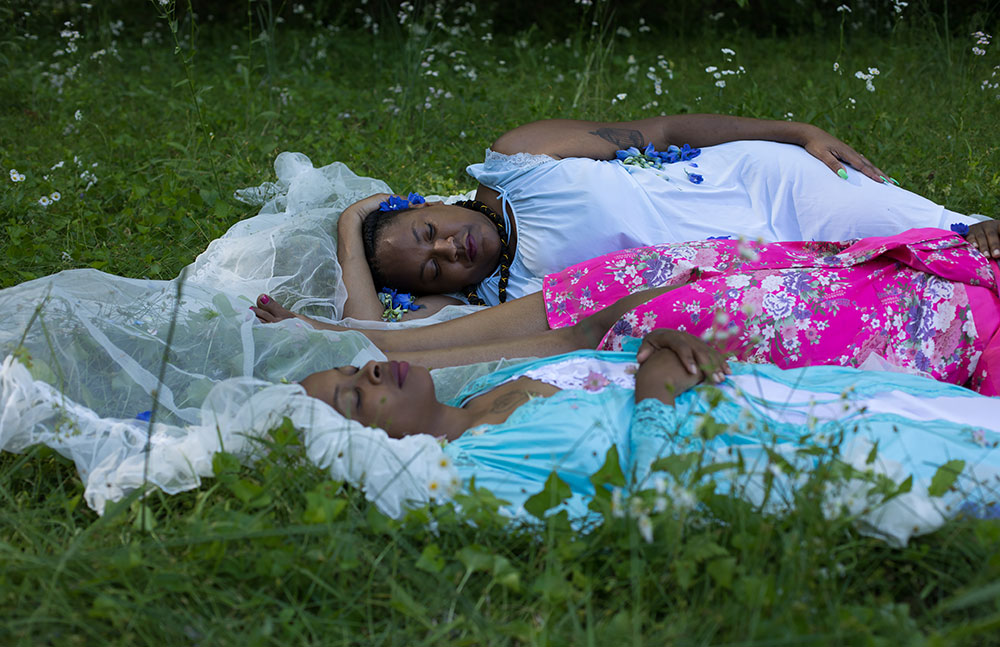 Three women wearing brightly colored dresses sleeping among plants.