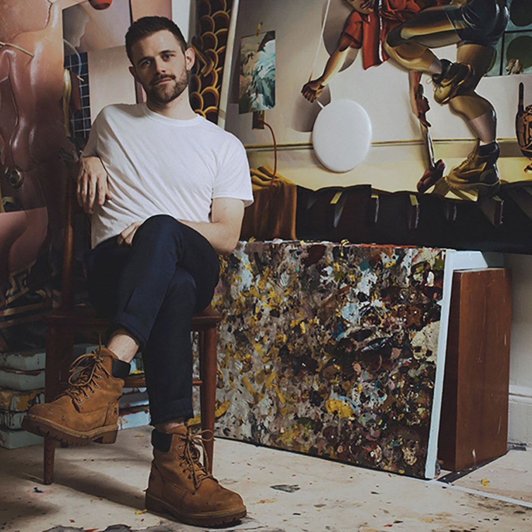 Artist Kyle Dunn sitting in his art studio with paintings next to him.