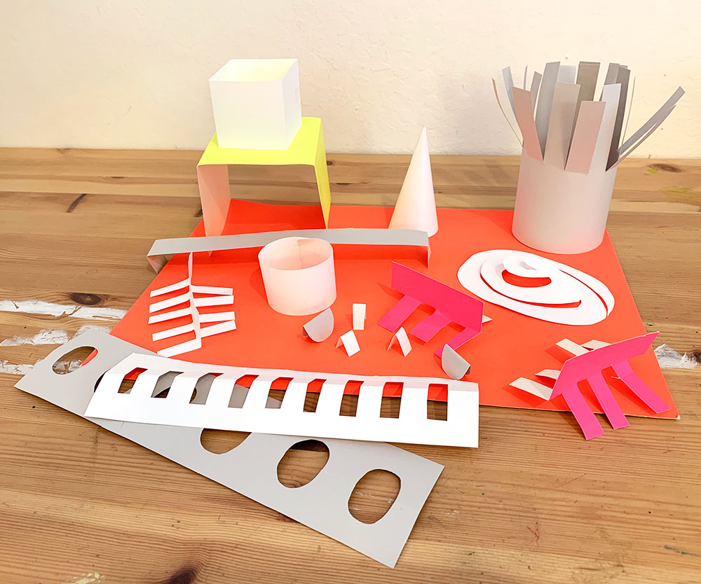 Brightly colored paper cut and folded into abstract shapes like cubes, tubes, and swirls.