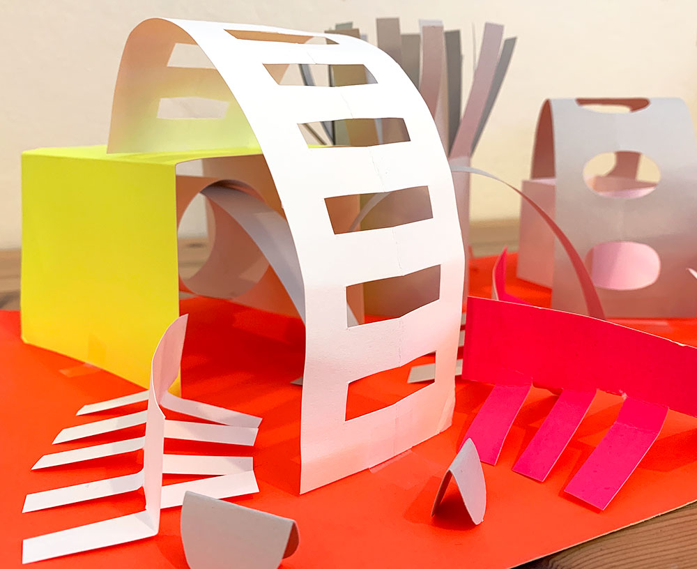 Brightly colored paper cut and folded into abstract shapes like cubes, tubes, and swirls.