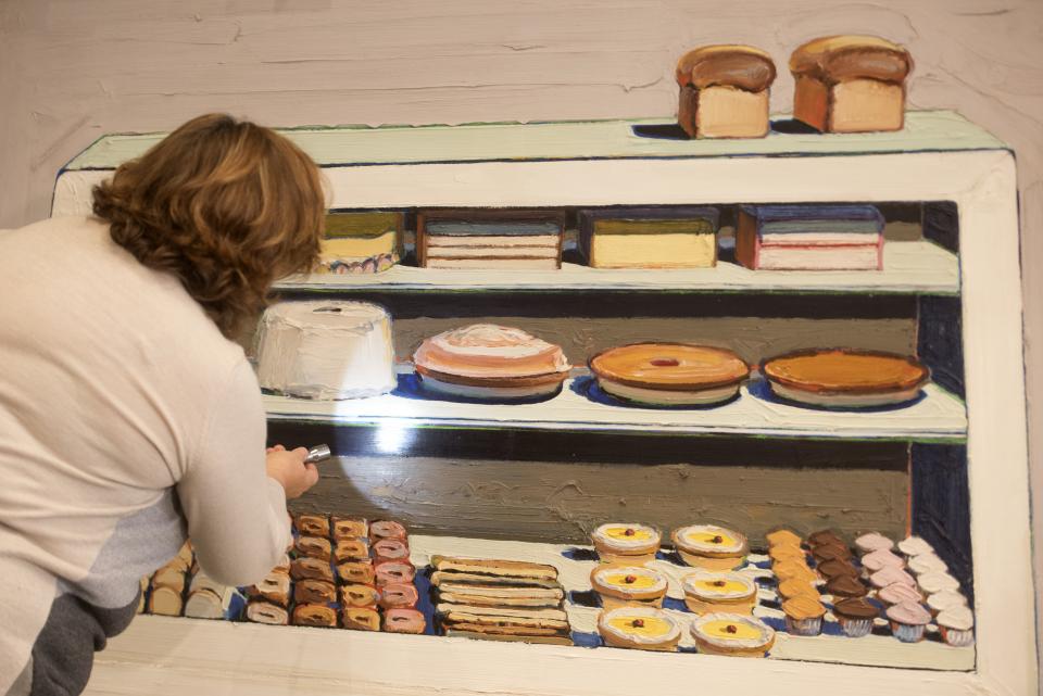 Photo of woman examining painting of cakes and pies in a bakery case.